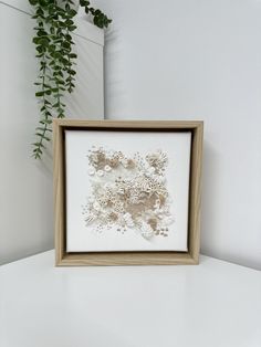 a white and brown framed artwork on a table next to a potted plant