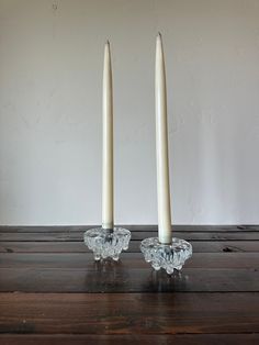 two white candles sitting on top of a wooden table