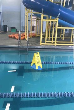 an empty swimming pool with water slide in the background and caution sign on the side