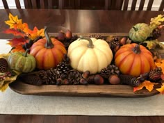 a wooden tray filled with pumpkins, pine cones and acorns on top of a table