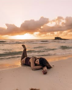 a woman laying on the beach with her feet up in the air as the sun sets