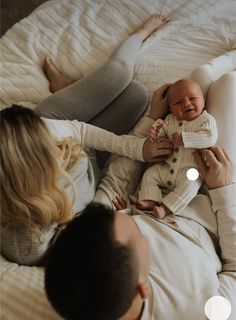 a man and woman laying on top of a bed holding a baby