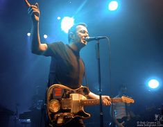 a man standing in front of a microphone while holding a guitar up to the air