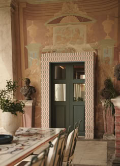 a dining room table and chairs in front of a green door with an ornate design on the wall