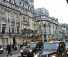 the cabs are lined up on the side of the road in front of tall buildings