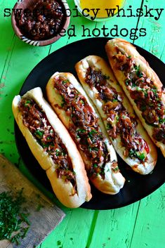 three hot dogs on a black plate next to some condiments