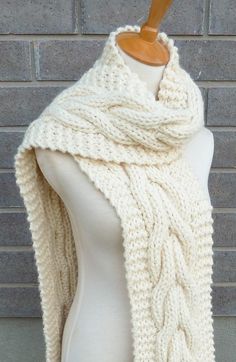 a white knitted scarf is on a mannequin with a brick wall in the background