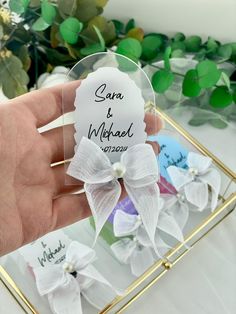 a hand holding a small personalized glass ornament with a bow on it