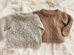 two sweaters sitting on top of a white furnishing covered bed next to each other