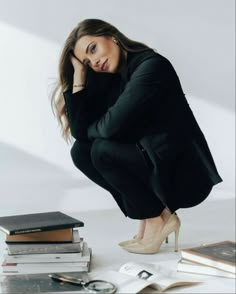 a woman kneeling down next to some books and a pair of high heeled shoes