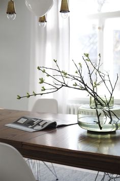 a wooden table topped with a glass vase filled with water and flowers next to a window