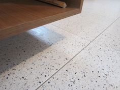 a close up of a wooden table on a tile floor with white speckles