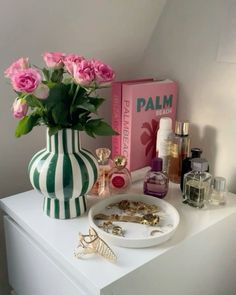 a white table topped with pink flowers next to a green and white vase filled with roses