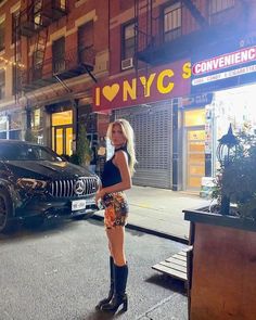 a woman standing on the street in front of a black car with her legs crossed