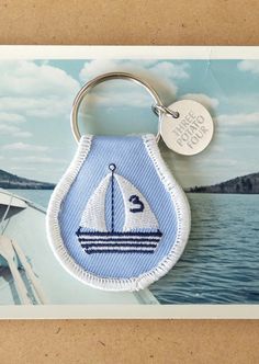 a blue and white sailboat keychain hanging from a hook on a card