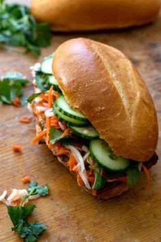 a sandwich with cucumbers and shredded carrots on a cutting board next to bread