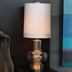 a glass lamp sitting on top of a wooden table next to a chair and painting