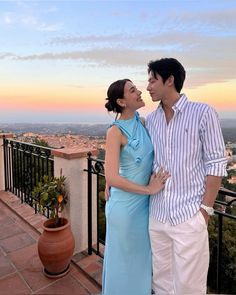 a man and woman standing next to each other on top of a balcony overlooking the city