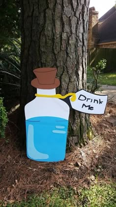 a sign attached to a tree that says drink me in front of a water bottle