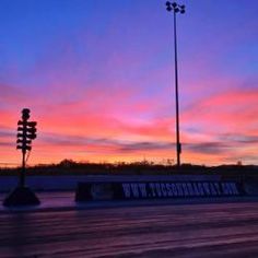 the sun is setting over an empty parking lot with lights on and street lamps in front of it