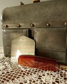 a brown comb sitting on top of a table next to a gray purse and mirror