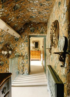 a hallway with floral wallpaper and stairs leading up to a mirror on the wall