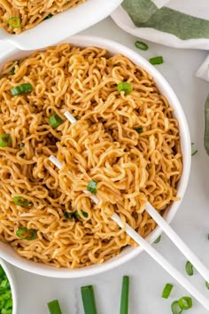 two bowls of noodles with chopsticks in them on a white surface, surrounded by green onions