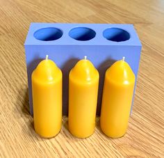 three yellow candles sitting in front of a blue box on a wooden table with four holes