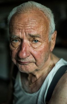 an older man with wrinkles on his face looking at the camera while wearing a white tank top