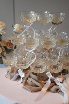 there are many wine glasses on the table with ribbons around them and flowers in the background