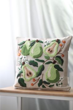 an embroidered pillow with pears on it sitting on a wooden table next to a white curtain