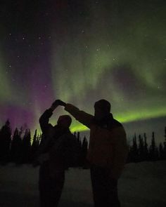 two people are standing in the snow with their arms around each other and looking up at the sky