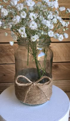 a mason jar filled with white flowers on top of a wooden table next to a wall