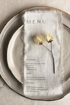 a plate with a menu on it and two flowers sitting on top of the table