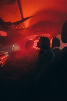 two people sitting in the back seat of a car with red light coming from behind them