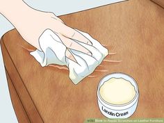 a person cleaning a wooden table with a cloth on it and a container of cream next to it