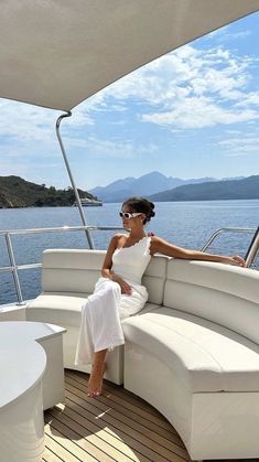 a woman is sitting on the back of a boat in the open water, wearing a white dress