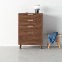 a wooden chest of drawers next to a blue towel on a stool in an empty room