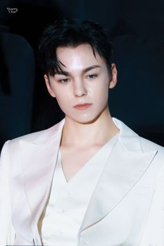 a young man with black hair and white shirt looking off to the side in front of a dark background