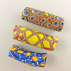 three different colored beads sitting next to each other on a white surface with blue, yellow and orange designs