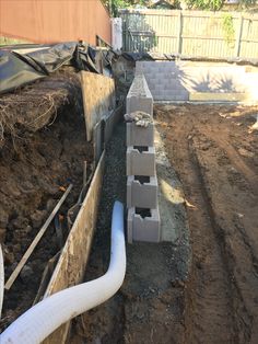 pipes are lined up along the side of a house under construction in an area with dirt and mud