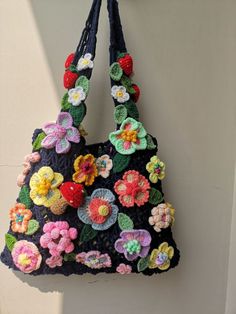 a crocheted purse hanging from a hook on a wall with flowers in it