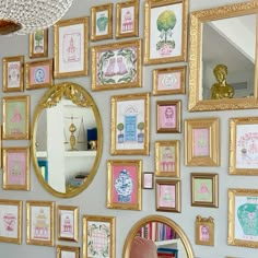 there are many framed pictures on the wall with gold frames and a pink chair next to it