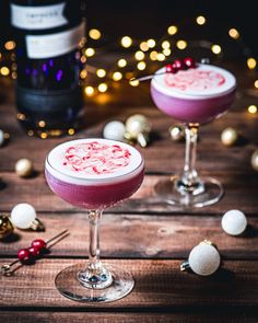 two glasses filled with pink and white liquid on top of a wooden table next to christmas decorations