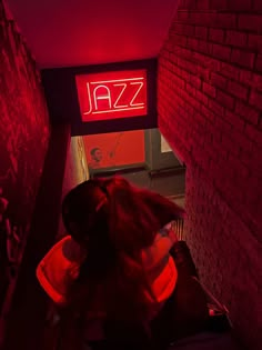 a woman is sitting on a chair in front of a neon sign that reads jazz