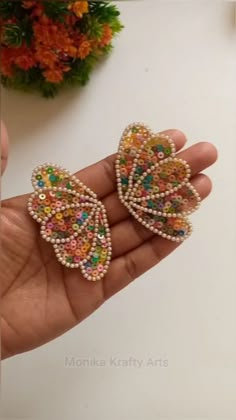 a hand holding two colorful butterfly shaped brooches