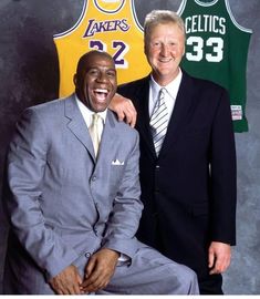 two men in suits and ties posing for a photo with a basketball jersey behind them