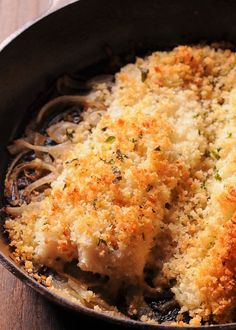 a skillet filled with pasta and meat covered in parmesan cheese crumbs