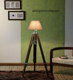 a tripod lamp sitting on top of a wooden floor next to a wall with pictures