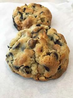 two chocolate chip cookies sitting on top of white paper